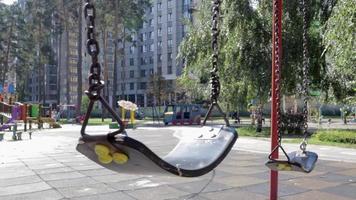 Close up empty baby swing in the park. New chain swing. Set of black swing chains on a modern playground. Focus on the swing in the blurry background. video