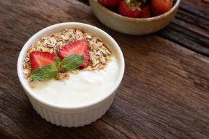 Strawberry yogurt in a wooden bowl with granola, mint and fresh strawberry on wooden background. Health food concept. photo