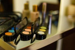 Two open compacts of colourful eye makeup on a table with assorted cosmetics including blusher, nail varnish and different brushes photo