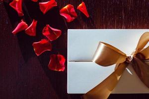 Gift box rose petals and decorative hearts on wooden background photo