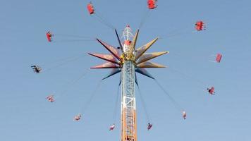 montar o carrossel alto no parque de diversões. as pessoas se divertem balançando em um balanço com uma corrente alta, aproveitam o passeio contra o céu azul. Ucrânia, Kharkiv - 17 de julho de 2021. video