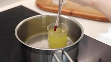 aqueça copos de água e óleo de jojoba em água fervente, registre a temperatura com um termômetro video