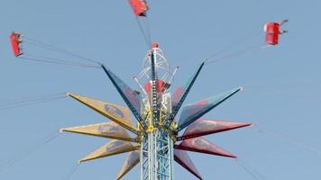 montar el carrusel alto en el parque de atracciones. la gente se divierte columpiándose en un columpio con una cadena alta, disfruta del paseo contra el cielo azul. ucrania, kharkiv - 17 de julio de 2021. video