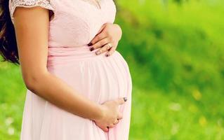 The pregnant girl in expectation of the kid, supporting a pregnant tummy with the hand, against the background of green trees photo