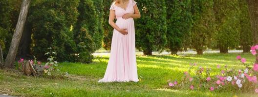 The pregnant girl in expectation of the kid, supporting a pregnant tummy with the hand, against the background of green trees photo