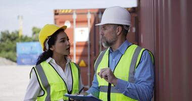 Handheld panning shot, middle-aged Caucasian business engineer man and pretty secretary female checking transport container, They are talking and write into report paper on clipboard at storage video