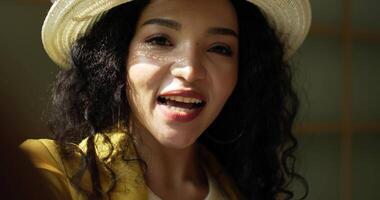 Handheld close up shot, Face of attractive young designer wearing stylish fashion hat smiling while using smartphone video call showing clothes during online sale in tailor shop