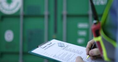 Handheld medium shot, Selective focus Hands of engineer man write on report paper on clipboard at storage container terminal video