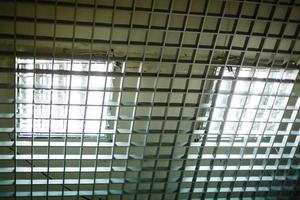 Two elevators inside white building at first floor with light on ceiling. Emergency telephone attached above button between elevators. Two fluorescent lamps in the ceiling grid photo