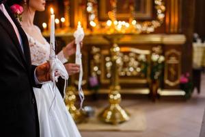 Newlyweds hold burning candles with pastel flowers during ceremony in church photo