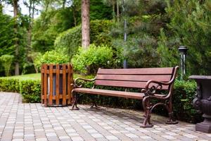 Forged wooden bench under the crown of trees in the city park on a sunny day. Perspective photo