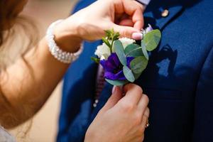 Close up bride's hands pinning boutonniere to groom' jacket photo