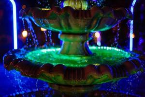small fountain with blue and yellow color illumination in the park photo