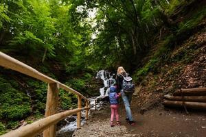 mother and daughter standing near the waterfall photo