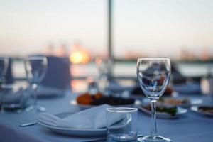 empty glass for wine almost a wooden table, on background of the sea, sunset sky and folded umbrellas photo