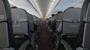 vista de pasillo estrecho dentro de la cabina del avión llena de pasajeros mientras se relaja, la gente viaja en avión con pasajeros irreconocibles en cómodos asientos de avión video