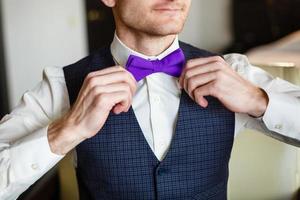 mariposa de color violeta en el cuello del hombre. el hombre viste una pajarita morada, morada. el novio yendo a la boda. mañana de bodas el hombre endereza su corbata. foto