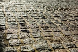 Black cobbled stone road background with reflection of light seen on the road. Black or dark grey stone pavement texture. Ancient paving stone background photo