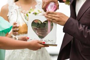 el novio y la novia vierten arena colorida en una caja con un corazón de cristal al aire libre foto