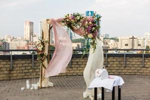 Beautiful wedding ceremony outdoors. Wedding arch made of cloth and white and pink flowers on the roof against the backdrop of a big city . Old doors, rustic style.