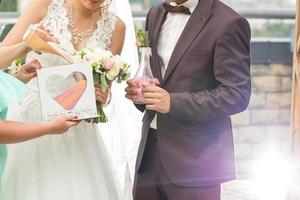 el novio y la novia vierten arena colorida en una caja con un corazón de cristal al aire libre foto