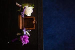 Wedding boutonniere. Gold rings lay in a wooden box. Purple white composition. photo