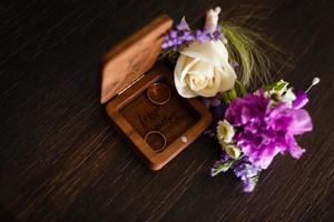 Wedding boutonniere. Gold rings lay in a wooden box. Purple white composition. photo