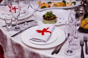 napkin tied with red ribbon on white empty plate on table. Table served for wedding banquet photo