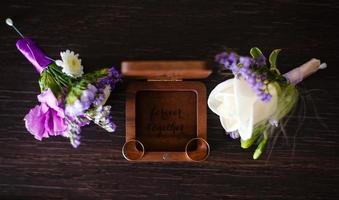 Wedding boutonniere. Gold rings lay in a wooden box. Purple white composition. photo