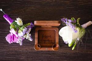 Wedding boutonniere. Gold rings lay in a wooden box. Purple white composition. photo