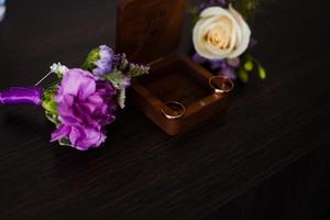 Wedding boutonniere. Gold rings lay in a wooden box. Purple white composition. photo