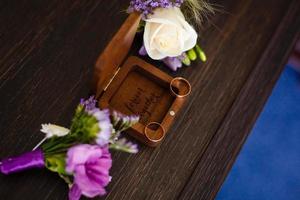 Wedding boutonniere. Gold rings lay in a wooden box. Purple white composition. photo