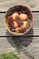 Easter eggs in a basket of 4 with pine leaves and pine cones on a light wooden background. photo