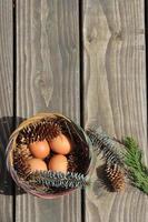 Easter eggs in a basket of 4 with pine leaves and pine cones on a light wooden background. photo