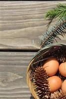Easter eggs in a basket of 4 with pine leaves and pine cones on a light wooden background. photo