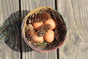 Easter eggs in a basket of 4 with pine leaves and pine cones on a light wooden background. photo