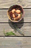 Easter eggs in a basket of 4 with pine leaves and pine cones on a light wooden background. photo