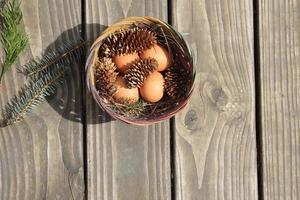 Easter eggs in a basket of 4 with pine leaves and pine cones on a light wooden background. photo