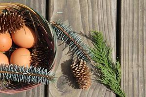 Easter eggs in a basket of 4 with pine leaves and pine cones on a light wooden background. photo