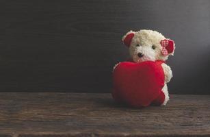 White teddy bears holding a heart shaped on dark wood floors.