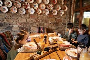 Four kids sit in authentic ukrainian restaurant, looking on phones. photo