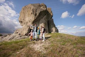 Family exploring nature. Children with parents wear backpack hiking against big stone in hill. Pidkamin, Ukraine. photo