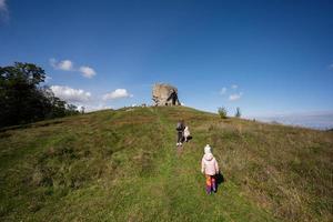 Kids exploring nature. Children wear backpack hiking near big stone in hill. Pidkamin, Ukraine.
