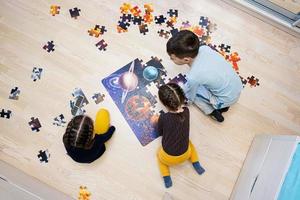 niños conectando piezas de rompecabezas en una habitación para niños en el piso en casa. diversión actividad familiar ocio. foto