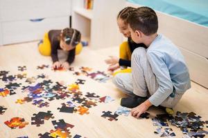 niños conectando piezas de rompecabezas en una habitación para niños en el piso en casa. diversión actividad familiar ocio. foto