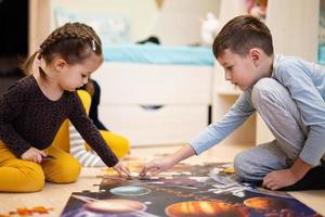 niños conectando piezas de rompecabezas en una habitación para niños en el piso en casa. diversión actividad familiar ocio. foto