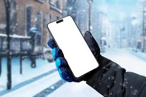 usando un teléfono móvil en la calle mientras está nevando. visualización aislada para la promoción de aplicaciones. mano de hombre sosteniendo un teléfono con un guante de invierno foto