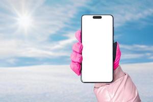 maqueta de teléfono en mano con guante rosa. nieve y sol de fondo. pantalla aislada con cámara para promoción de aplicaciones foto