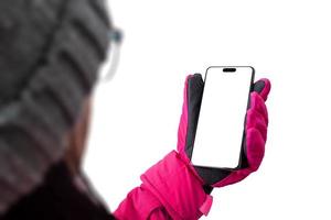 chica sostiene un teléfono móvil con equipo de esquí. chaqueta de invierno rosa con guantes y gorro. concepto de usar un teléfono en una pista de esquí. pantalla aislada y fondo para la presentación de aplicaciones y páginas web foto