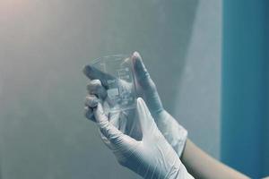 manos enguantadas sosteniendo un vaso de precipitados vacío en el laboratorio foto